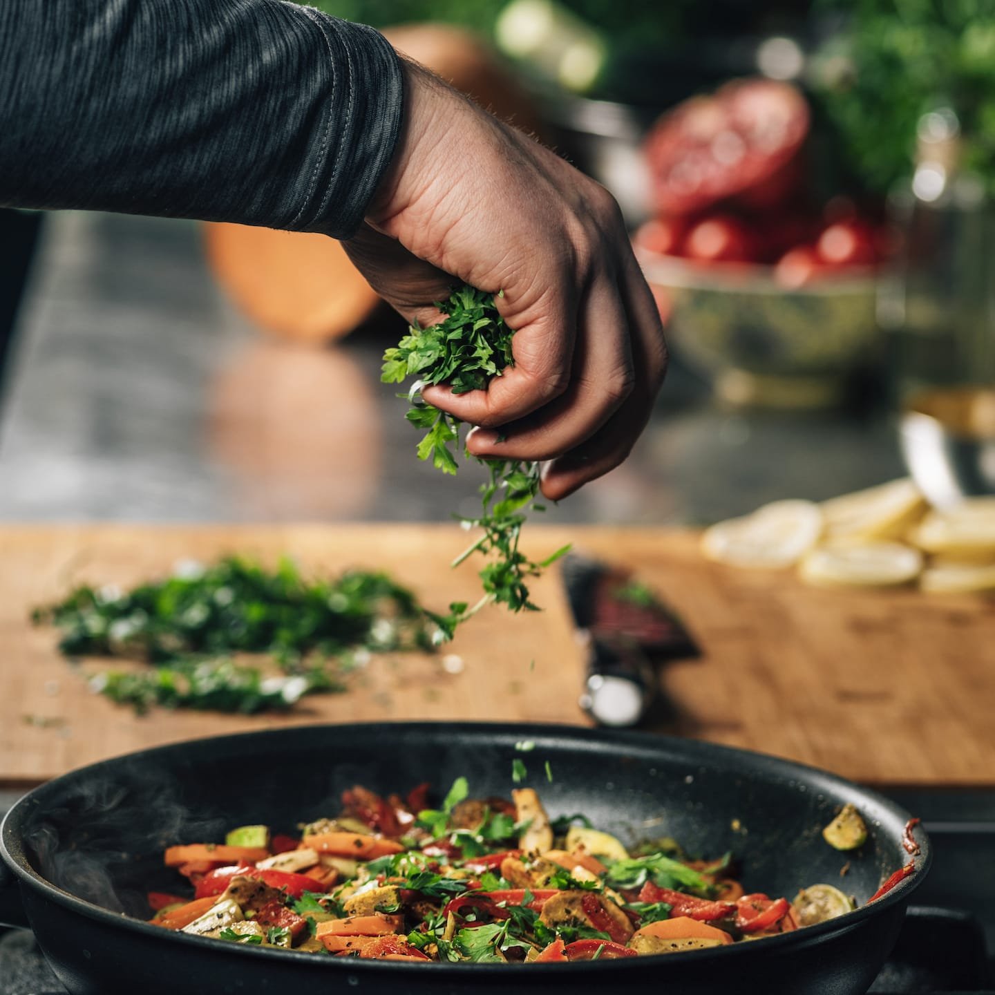 hand adding parsley into frying pan with vegetable